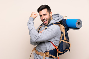 Wall Mural - Young mountaineer man with a big backpack over isolated background making strong gesture