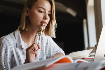 Canvas Print - Photo of focused young woman making notes and using laptop