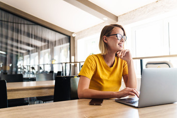 Sticker - Photo of joyful young woman using laptop and smiling while sitting