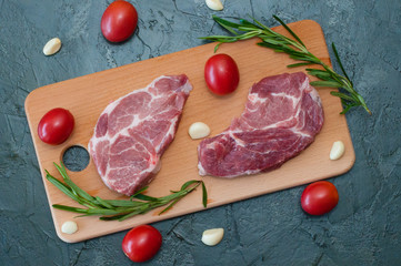 Wall Mural - Flat lay, raw meat pork steak with tomatoes garlic and rosemary on a wooden cutting board top view