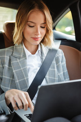 Wall Mural - Image of businesslike woman using laptop inside car on passenger seat