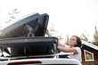 © koldunova - Woman opens the trunk or cargo box, which is located on the roof of the car. Preparing for a vacation.