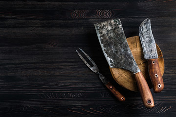 Old butcher meat knife, cleaver and fork on black background