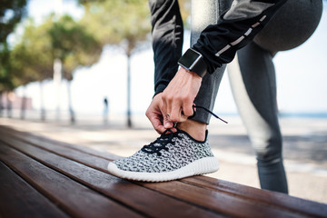 Wall Mural - A young sportswoman with smartwatch outdoors in city, tying shoelaces.