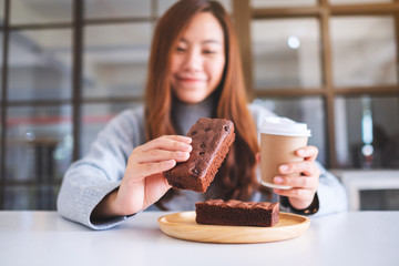 Wall Mural - Closeup image of a beautiful woman holding and eating a piece of brownie cake while drinking coffee