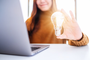 Wall Mural - closeup image of a businesswoman holding and showing a glowing light bulb while working on laptop