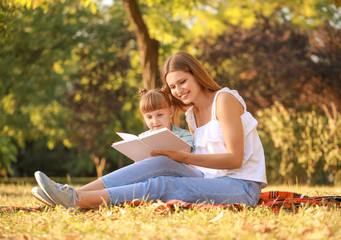 Sticker - Beautiful young woman and her little daughter reading book in park