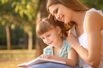 Sticker - Beautiful young woman and her little daughter reading book in park