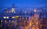 Fototapeta Londyn - Prague Czech Republic. View at nighttime winter town with falling snow tower and broach cathedral. Illuminated with illumination street and Church of Our Lady Before Tyn aerial view.