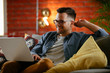© JustLife - Young man working from home. Businessman sitting on sofa and using laptop.