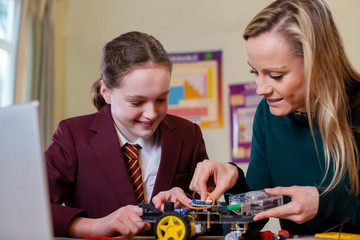 Wall Mural - Teacher Helping Female Pupil Wearing Uniform To Build Robot Car In Science Lesson