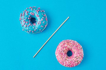 Two donuts separated with a drinking straw on blue background. Creative food concept