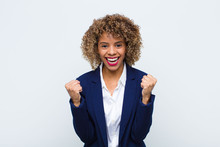 Young Woman African American Feeling Shocked, Excited And Happy, Laughing And Celebrating Success, Saying Wow! Against Flat Wall