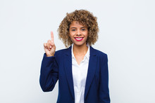 Young Woman African American Smiling Cheerfully And Happily, Pointing Upwards With One Hand To Copy Space Against Flat Wall