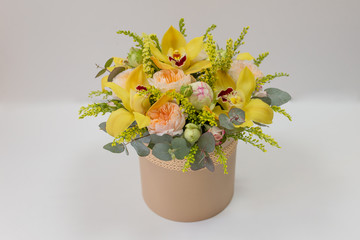 composition of fresh flowers in yellow colors (rose, orchid, peony, eucalyptus) in a beige hat box on a light background