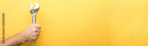 Fotografía panoramic shot of man holding spanner on yellow background