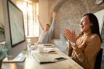 Asian businesswoman celebrating achievement while using desktop PC in the office.