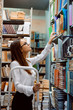 Young attractive female librarian worker standing on the ladder checking books, their condition and presence