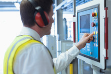 Worker With Ear Protectors At Control Panel In Machinery 