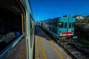 Wall Mural - An older italian commuter train is waiting on a train platform, waiting for the other train to pass by. Older vintage style train of italian railways.