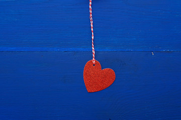 paper red shiny decorative hearts hanging on a rope on a dark blue wooden background