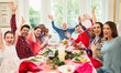 © Robert Daly/Caia Image - Portrait enthusiastic multi-ethnic multi-generation family waving at Christmas dinner table