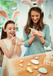 © Robert Daly/Caia Image - Mother and daughter wearing costume rabbit ears decorating Easter eggs
