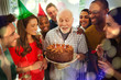 © Robert Daly/Caia Image - Multi-ethnic family watching senior man blow out birthday candles on chocolate cake
