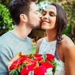© Robert Daly/Caia Image - Affectionate man giving red rose bouquet to girlfriend, kissing her on cheek
