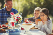 © Paul Bradbury/Caia Image - Father watching daughters eating at sunny garden party patio table