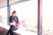 © Trevor Adeline/Caia Image - Businesswoman using digital tablet drinking coffee at sunny urban office window