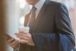 © Martin Barraud/Caia Image - Close up businessman in suit with coffee texting with cell phone