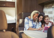 © Paul Bradbury/Caia Image - Smiling mother and daughters using digital tablet inside motor home