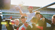 © Chris Ryan/Caia Image - Formula one racing team carrying driver trophy on shoulders, celebrating victory