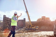© Trevor Adeline/Caia Image - Construction worker foreman using walkie-talkie directing crane at sunny construction site
