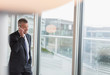© Martin Barraud/Caia Image - Businessman talking on cell phone at office window