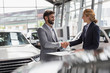 © Martin Barraud/Caia Image - Car saleswoman male customer handshaking in car dealership showroom