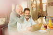 © Tom Merton/Caia Image - Male gay couple using laptop at breakfast kitchen counter