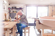 © Agnieszka Olek/Caia Image - Male carpenter working at laptop on workbench near wood boat in workshop
