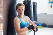 © Sam Edwards/Caia Image - Portrait confident, tough female boxer wrapping wrists next to punching bags in gym