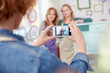 © Agnieszka Olek/Caia Image - Woman camera phone photographing classmates posing at painted side table in art class workshop
