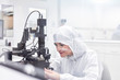 © Rafal Rodzoch/Caia Image - Female engineer in clean suit using equipment in fiber optics research testing laboratory