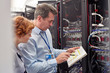 © Rafal Rodzoch/Caia Image - IT technicians with clipboard examining panel in server room