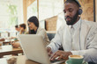 © Caiaimage/Paul Bradbury/Caia Image - Young man with headphones using laptop drinking coffee at cafe table