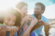 © Sam Edwards/Caia Image - Happy family eating baguette sandwiches on sunny summer beach