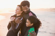 © Sam Edwards/Caia Image - Affectionate multi-ethnic family in wet suits hugging on sunset beach