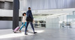 © Caiaimage/Martin Barraud/Caia Image - Businessman businesswoman walking, pulling suitcase in modern office lobby