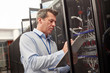 © Rafal Rodzoch/Caia Image - Male IT technician writing on clipboard at panel in server room