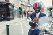 © Caiaimage/Paul Bradbury/Caia Image - Smiling young businessman in helmet on motor scooter texting cell phone on urban street