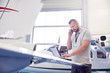 © Agnieszka Olek/Caia Image - Male airplane mechanic talking on cell phone working at laptop in hangar